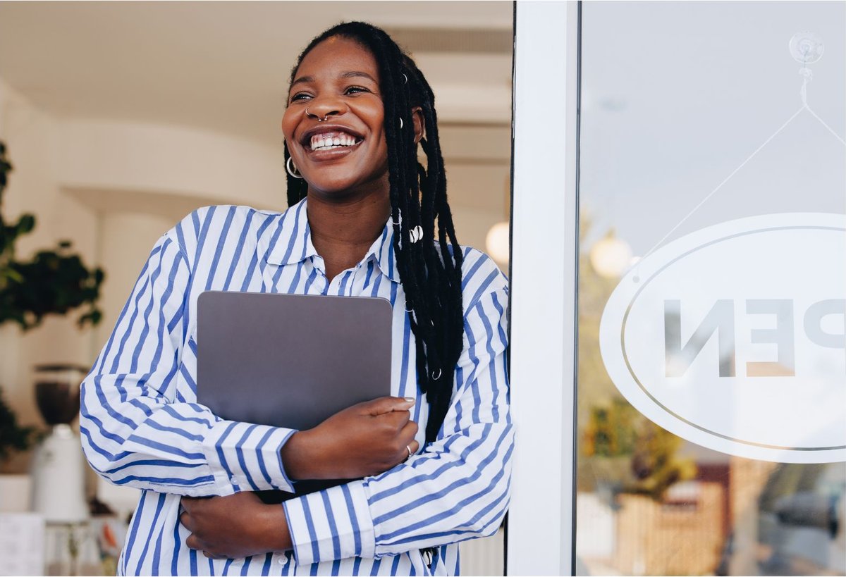 A small business owner smiling in her shop doorway, tablet in hand